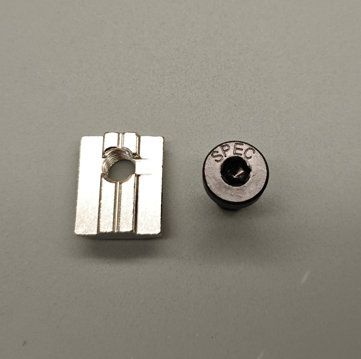 SPEC wide-wing T-nut and SPEC-engraved M8 socket-head bolt, top view, on grey