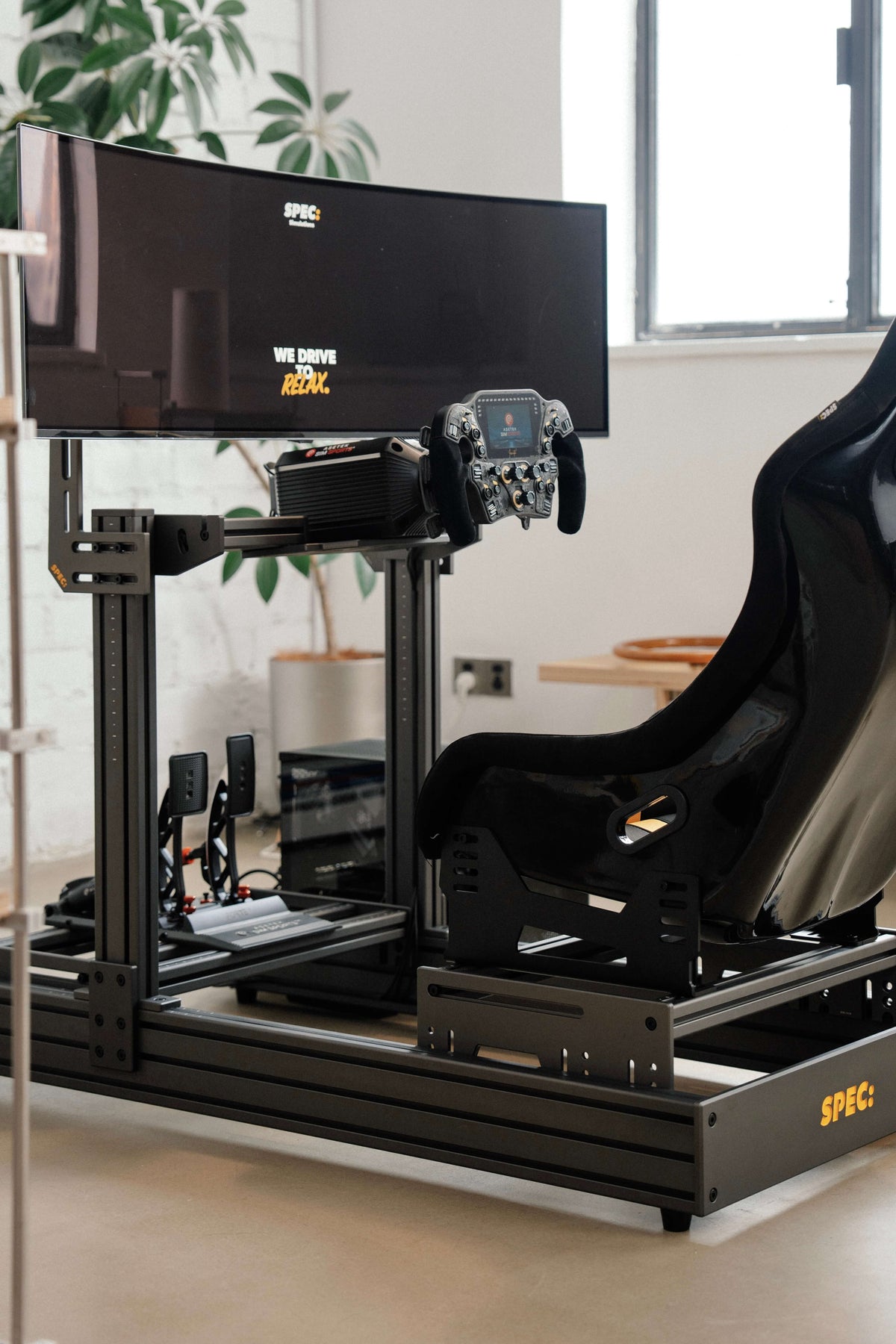 SPEC 282 sim rig, black frame, in a living room beside a window and a plant