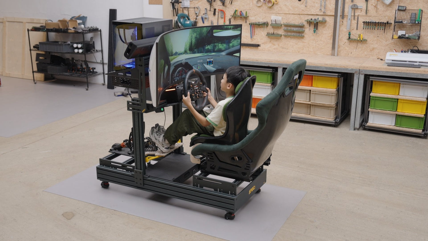 A child driving a SPEC 282 with the Growth Kit fitted, child seat ahead of the adult seat and pedal platform on the base, in the SPEC workshop.